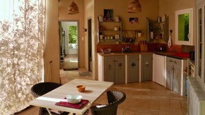 A kitchen with wooden cabinets, a dining table with chairs, and a view through an open door to a balcony. - Sous L'olivier Avec Piscine Privative (Buisson)