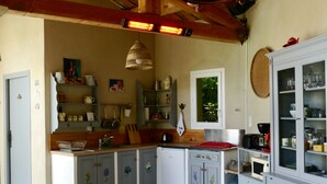 A kitchen with a dining area, wooden beams, a hanging light fixture, and a window with greenery outside. - Sous L'olivier Avec Piscine Privative (Buisson)