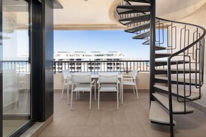 A balcony with a spiral staircase, white chairs, and a view of buildings.