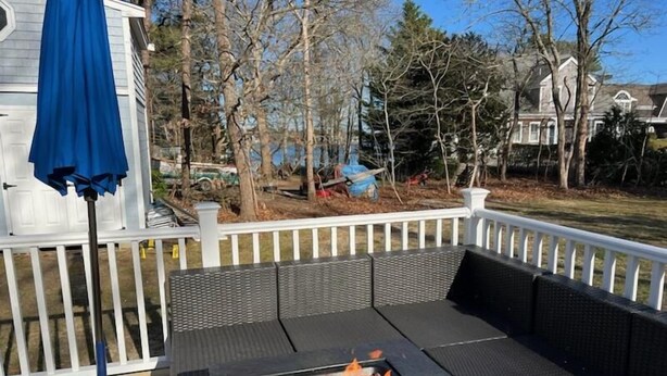 A deck with a fire pit, outdoor seating, and a blue umbrella. - Cozy Cottage walk to Menauhant Beach (East Falmouth)