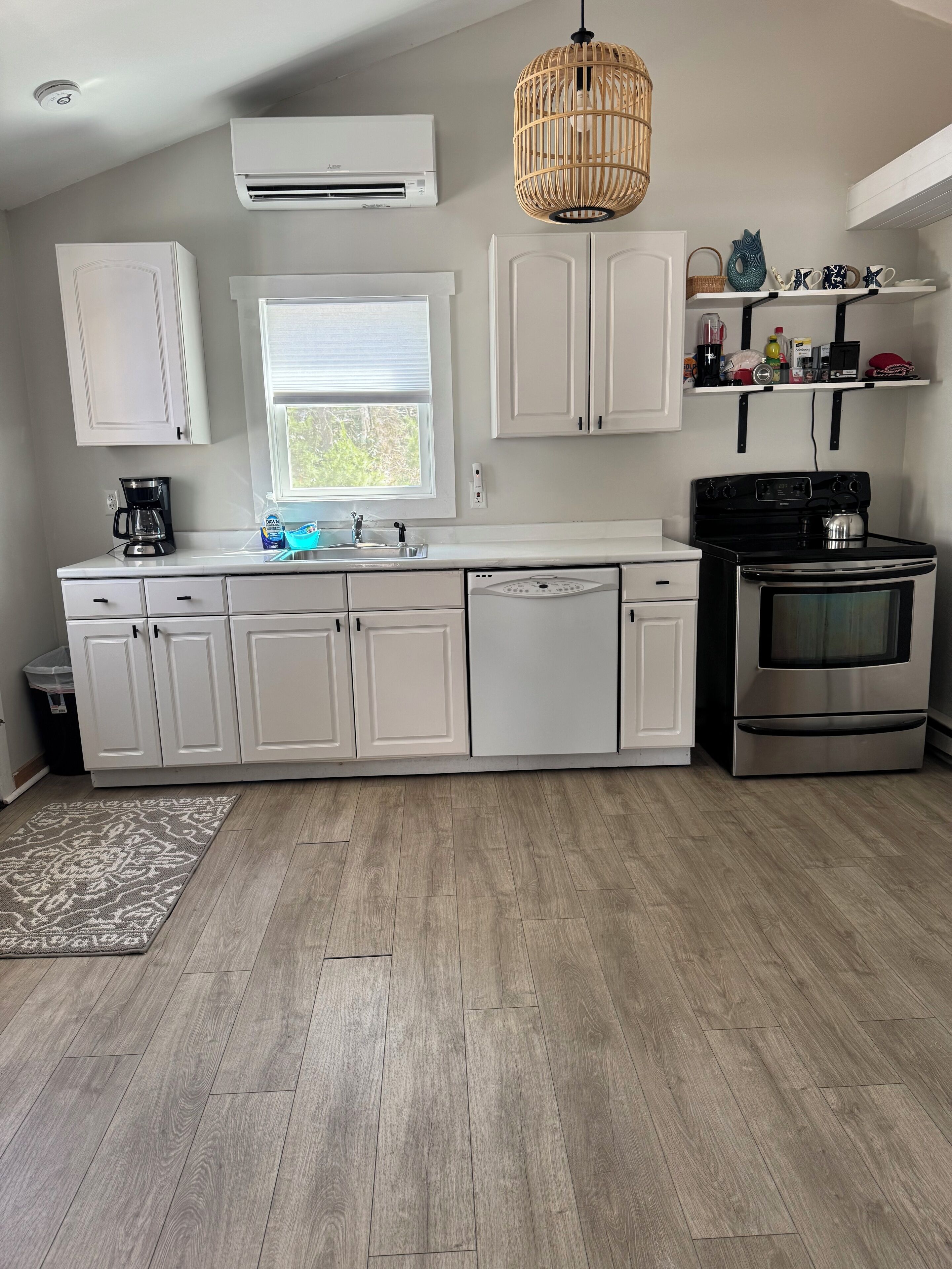 Une cuisine moderne avec des meubles blancs, un lave-vaisselle encastré, une cuisinière et un luminaire suspendu.