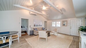 A spacious living area with a high ceiling, a dining table with chairs, a sofa, and a large rug. - Cozy Cottage walk to Menauhant Beach (East Falmouth)