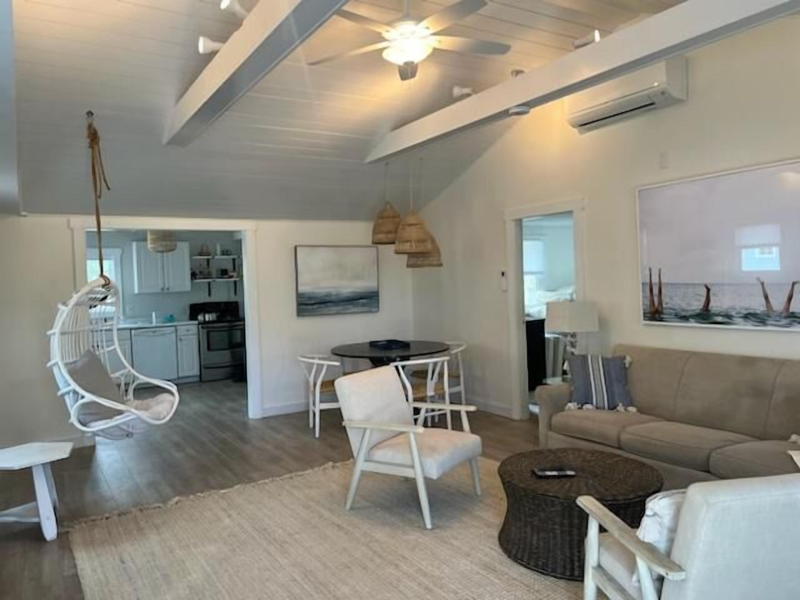 A modern living room with a dining area, a hanging chair, and a view of the kitchen.