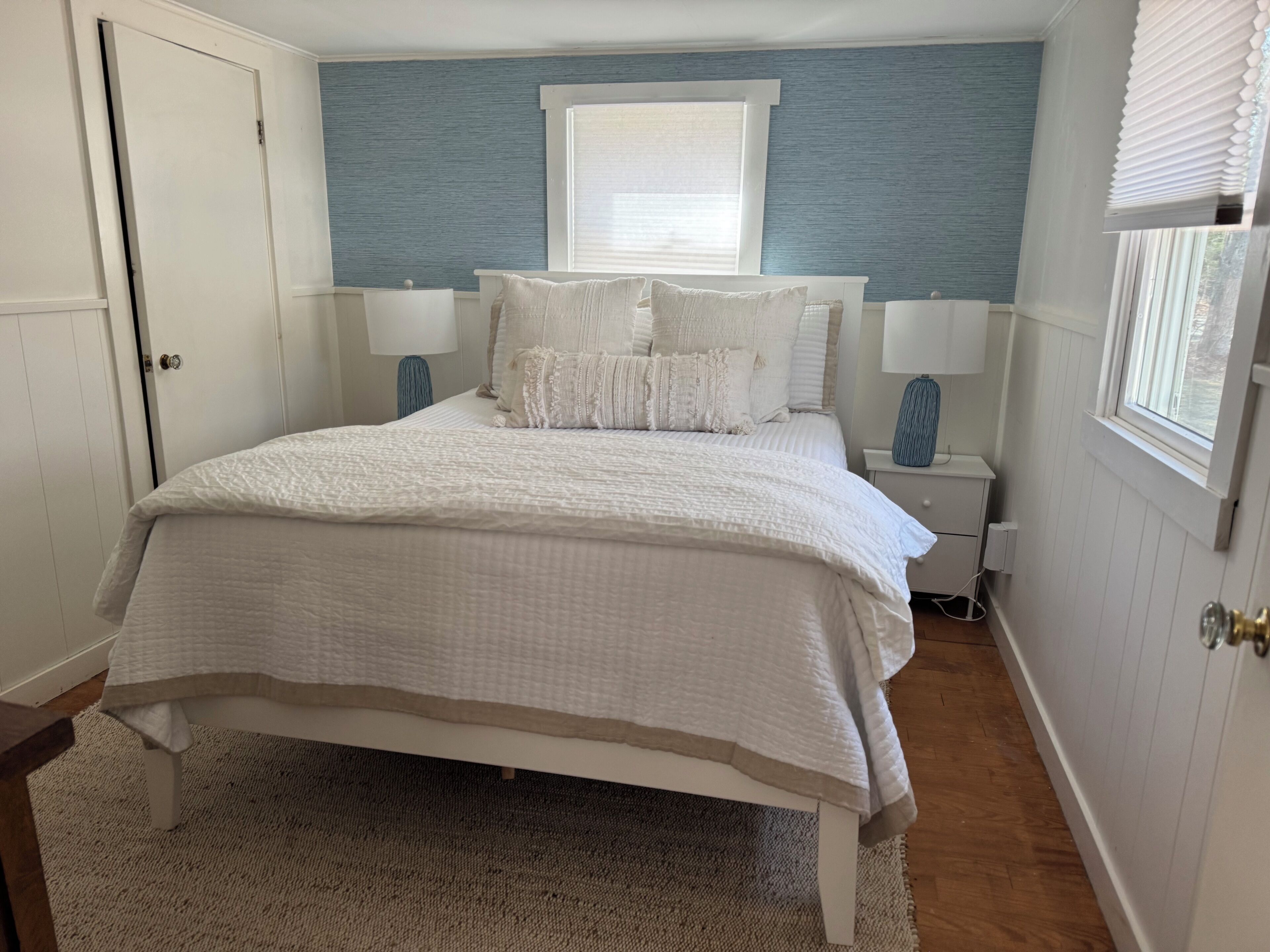 A bedroom with a bed, two bedside tables, a window, and a door.