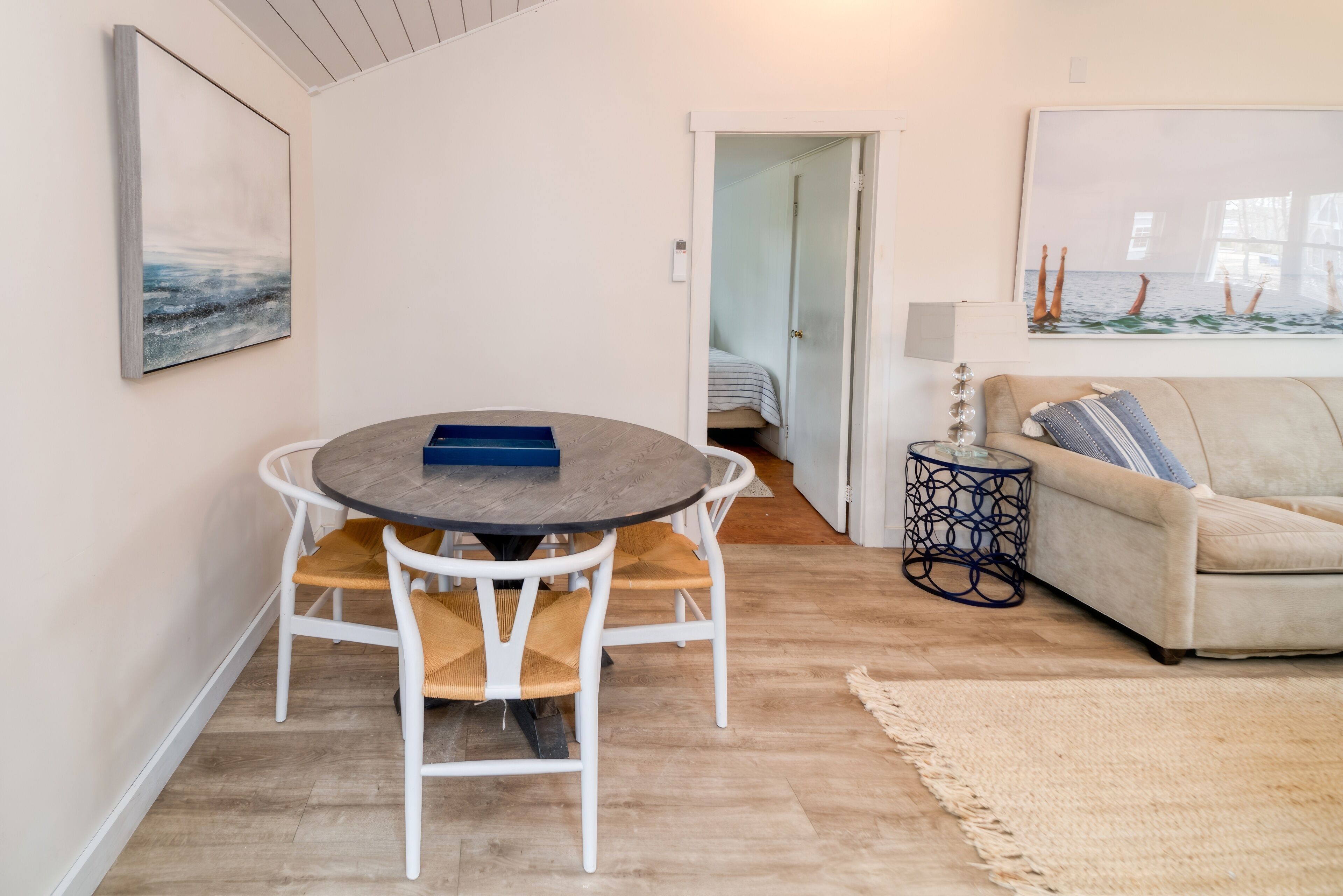 A living room with a round table, white chairs, a beige sofa, and a painting on the wall.