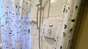 A shower with a handheld showerhead, a wall-mounted control panel, and a shower curtain with a speckled pattern. - Ninalodge - Cosy, private self-contained apartment (Letterkenny)