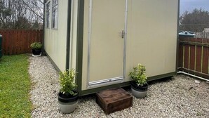 A small, single-story shed with a door and windows, surrounded by gravel and potted plants. - Ninalodge - Cosy, private self-contained apartment (Letterkenny)