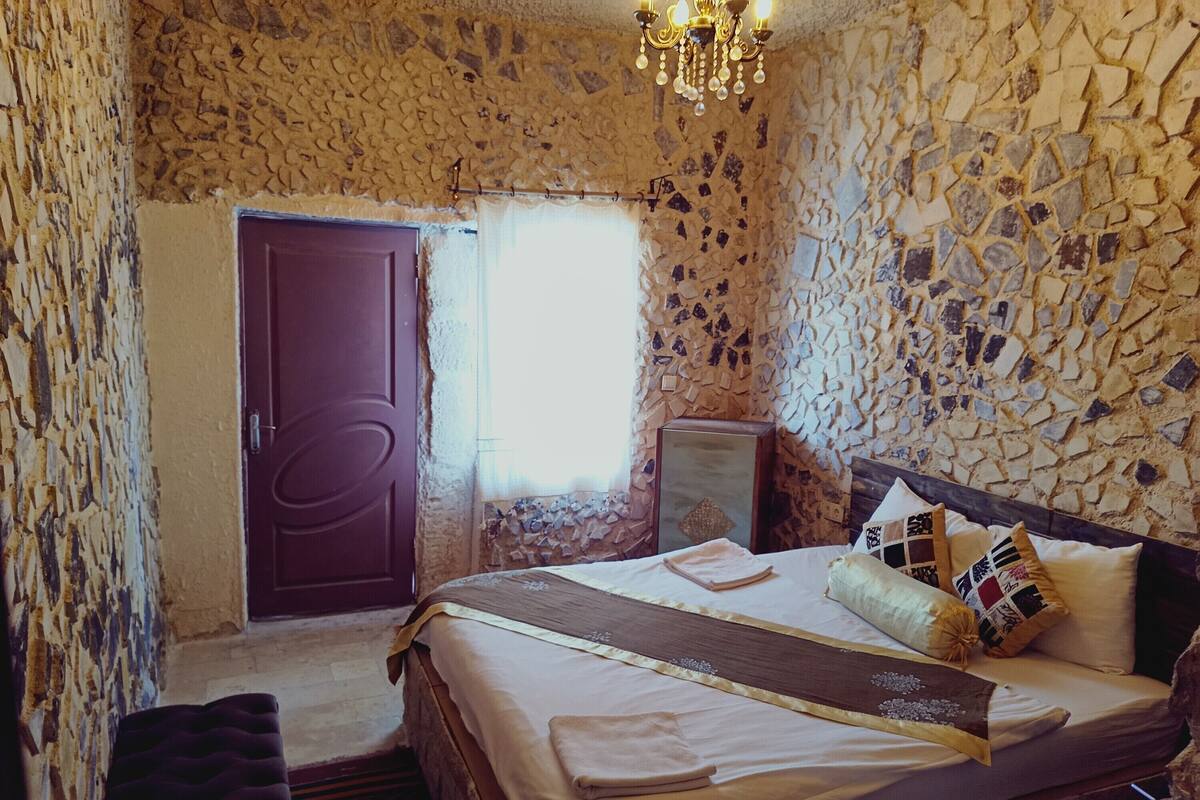 Une chambre avec un mur en pierre, un lit en bois, une table de chevet et un lustre.
