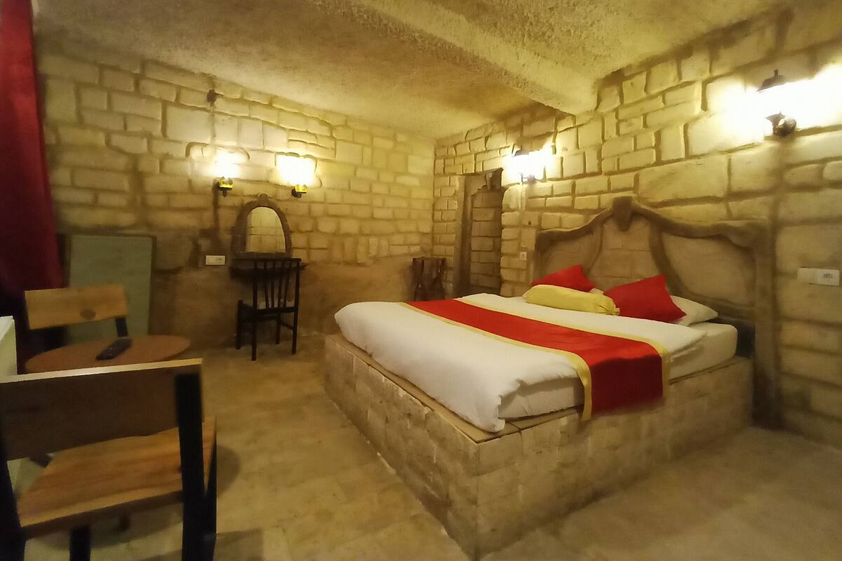 Une pièce avec un mur en pierre, un lit avec une literie rouge et blanche, une chaise en bois et une petite table avec un miroir.