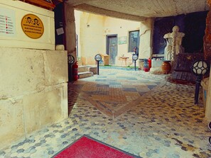 A corridor with patterned flooring, a red mat, a statue, and a plaque with a health message. - Stone Age Mansion (Ürgüp)
