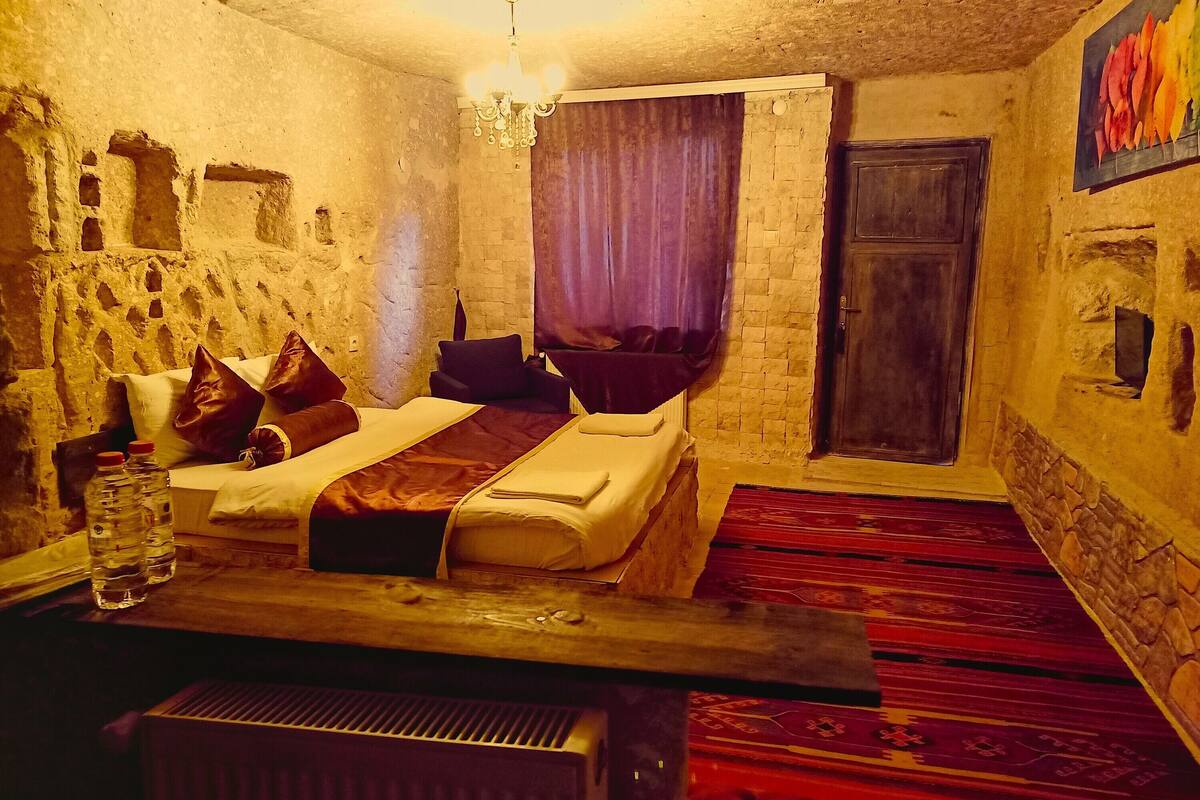 Une pièce comprenant un lit, des oreillers, une bouteille d’eau, un radiateur, un lustre et une porte.