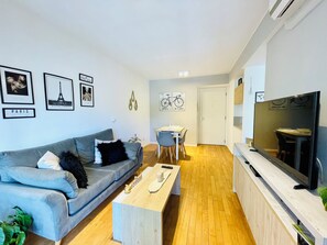 A modern living room with a grey sofa, a wooden coffee table, and a dining area with a white table and chairs.