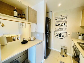 A modern kitchen with a white countertop, a coffee machine, and a refrigerator. There is a wall decoration with text and a coffee cup. - Stylish Apartment with Pool Acces (Buenos Aires)