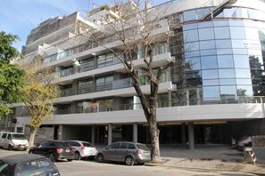 A multi-story building with a glass facade, parked cars, and a tree in front. - Stylish Apartment with Pool Acces (Buenos Aires)