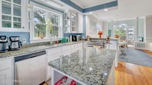 A modern kitchen with granite countertops, white cabinetry, and a large island. - 2nd Row, Private Pool and Jacuzzi! (Kure Beach)