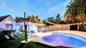 Un jardin avec une piscine, des chaises longues et des guirlandes lumineuses.