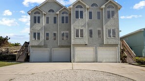 A two-story residential building with a symmetrical facade, multiple garage doors, and a staircase leading to the upper level.