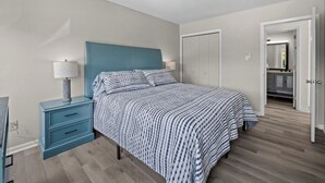 A bedroom with a bed, nightstand, lamp, ceiling fan, and a door leading to a bathroom.