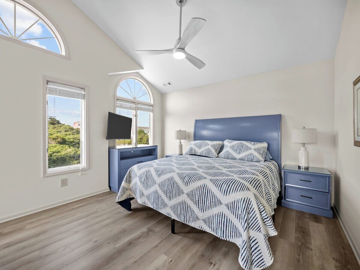 Una camera da letto con un letto, un comodino, una ventola a soffitto e due finestre.