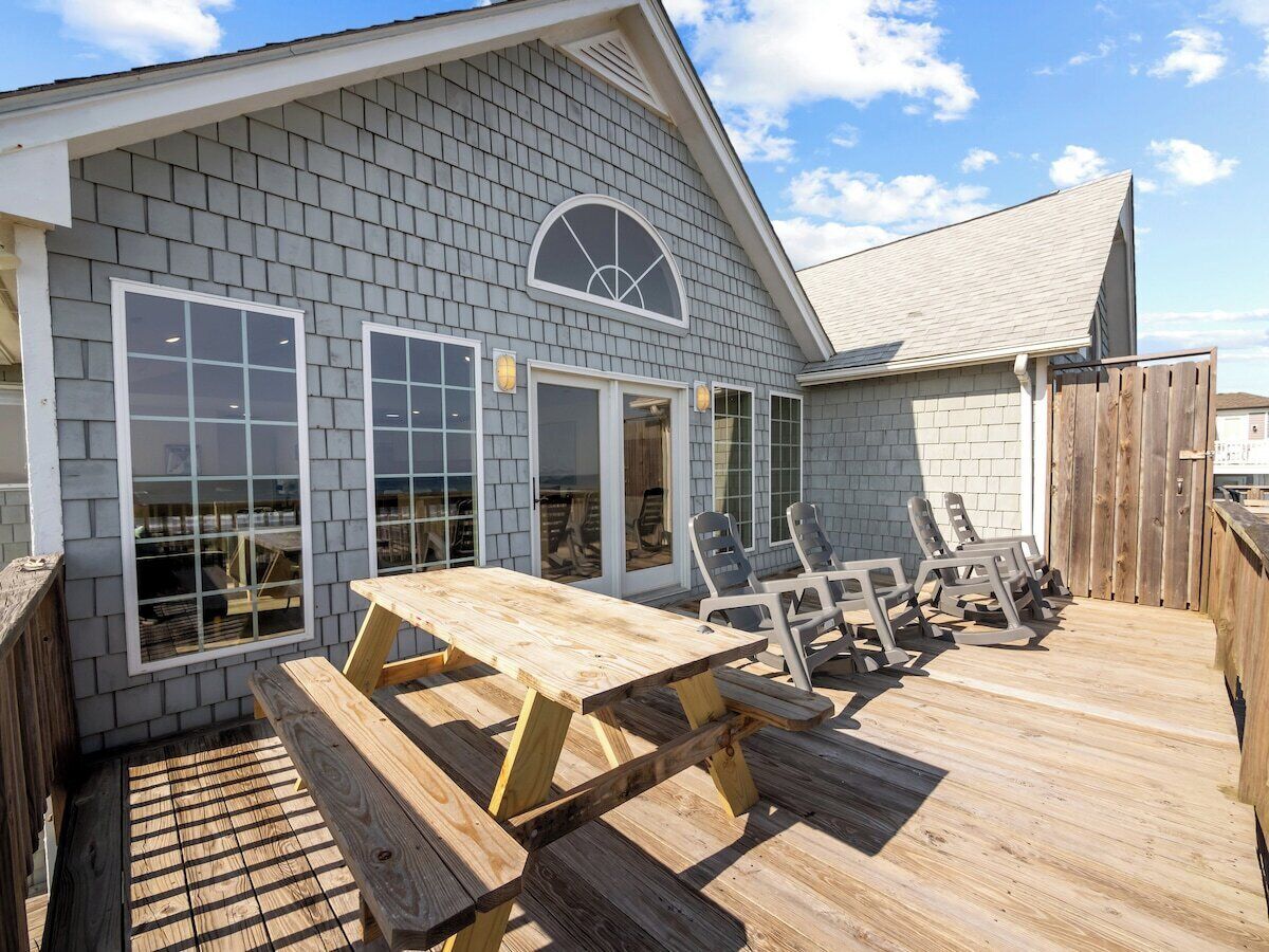 A wooden deck with a picnic table and chairs, a covered area with a window, and a wooden fence.