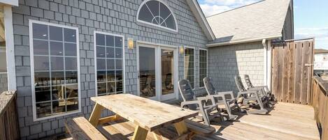 A wooden deck with a picnic table and chairs, a covered area with a window, and a wooden fence.