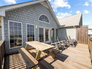 A wooden deck with a picnic table and chairs, a covered area with a window, and a wooden fence.