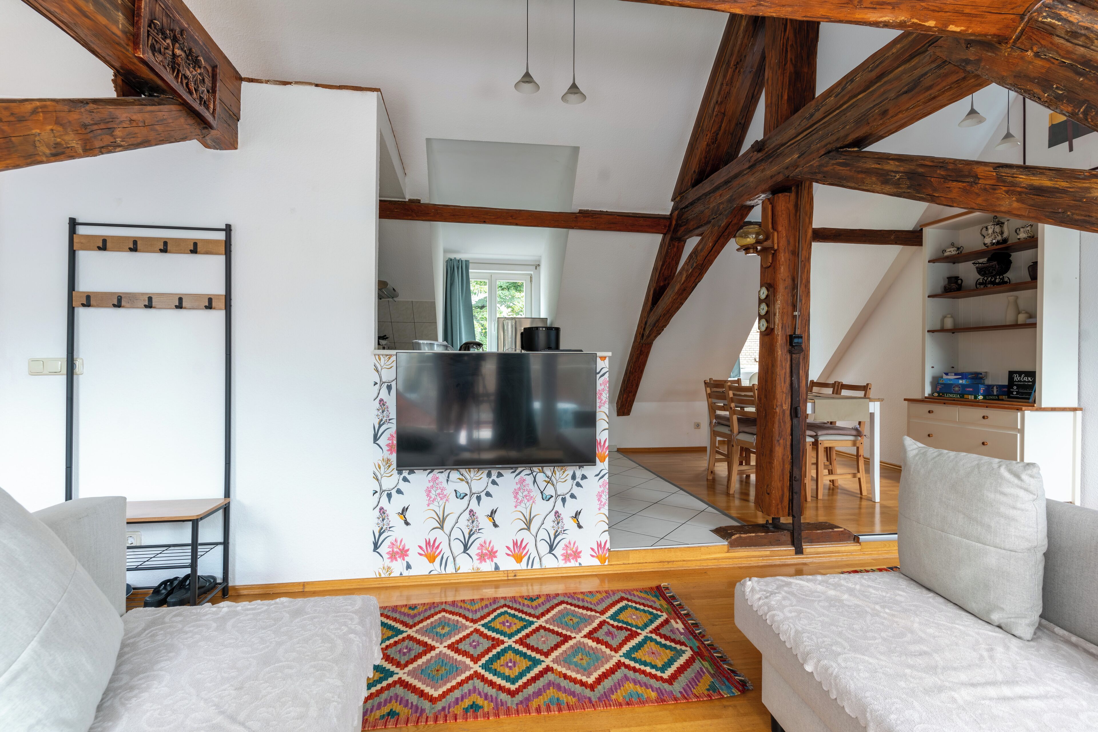 Un salon chaleureux avec un canapé, un tapis aux couleurs vives et un téléviseur fixé au mur, au-dessus d’un meuble orné de motifs floraux.