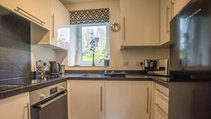 Una cocina moderna con armarios blancos, encimera negra, refrigerador de acero inoxidable y una ventana con vista a la vegetación.
