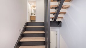 A staircase with wooden steps and metal railings leading to a room with a white door and a kitchen area visible in the background.