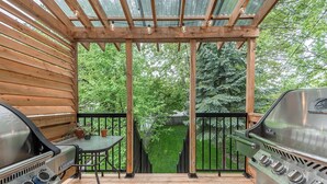 A covered outdoor patio with two barbecue grills, a table, and a bench.