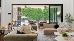 Een moderne woonkamer met een grote schuifglazen deur die uitkomt op een weelderige groene tuin.