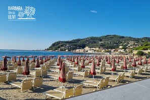 A beach with rows of sun loungers and umbrellas, a clear blue sky, and a hillside in the background. - BARBARA TRA GLI ULIVI - An oasis of peace for a holiday dedicated to good living (Diano Arentino)