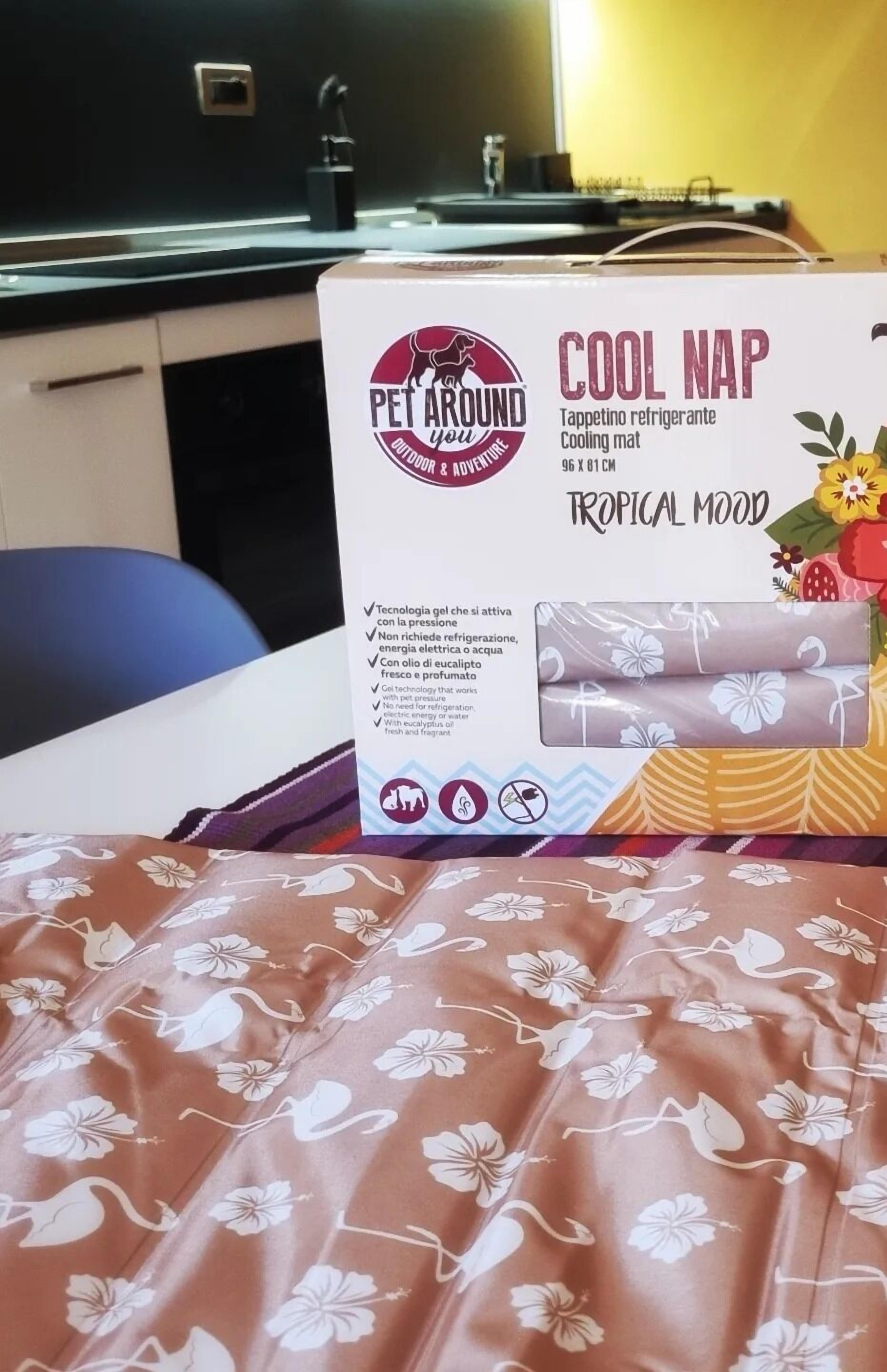 A box of 'Cool Nap' cooling mat with a floral pattern, placed on a bed with a similar floral bedspread.