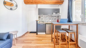 Una cocina compacta con techo de madera, una zona de comedor con taburetes, un sofá y un reloj de pared.