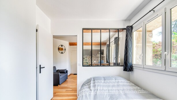 Un dormitorio con cama, ventana con cortinas, puerta y vista a un comedor.