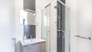 Un baño moderno con ducha envuelta en vidrio, un lavamanos blanco y un espejo encima.