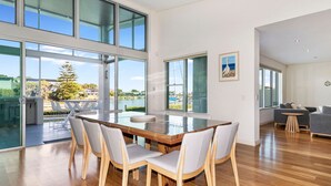 Un vaste espace dédié à la salle à manger, avec une grande table et des chaises, de grandes fenêtres offrant une vue sur un plan d’eau et la verdure, et un aménagement intérieur moderne.