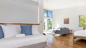 Une chambre d’hôtel moderne dotée d’un grand lit, d’un canapé, d’une petite table et d’un balcon offrant une vue sur la verdure.