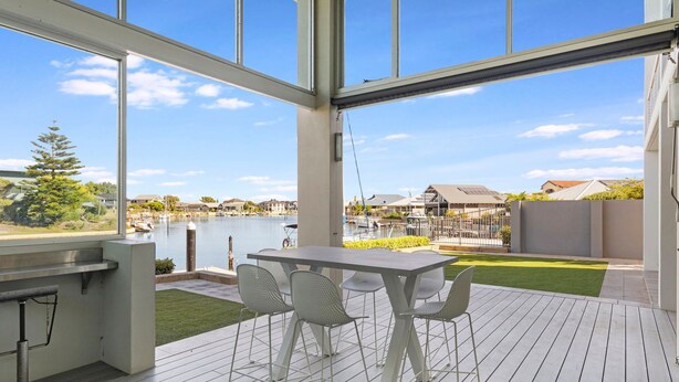 Une terrasse extérieure moderne, dotée d’une table et de chaises, qui offre une vue sur un port de plaisance et des immeubles résidentiels.