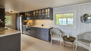 A modern kitchen with grey cabinets, a large island, and a view of the sea through a window.