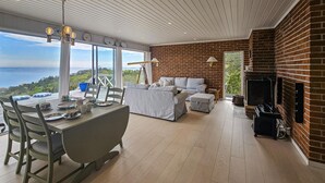 A modern living room with a large window overlooking a scenic view, a fireplace, and a dining area with a table set for two.