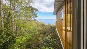 A wooden house with a view of the sea and surrounding trees.