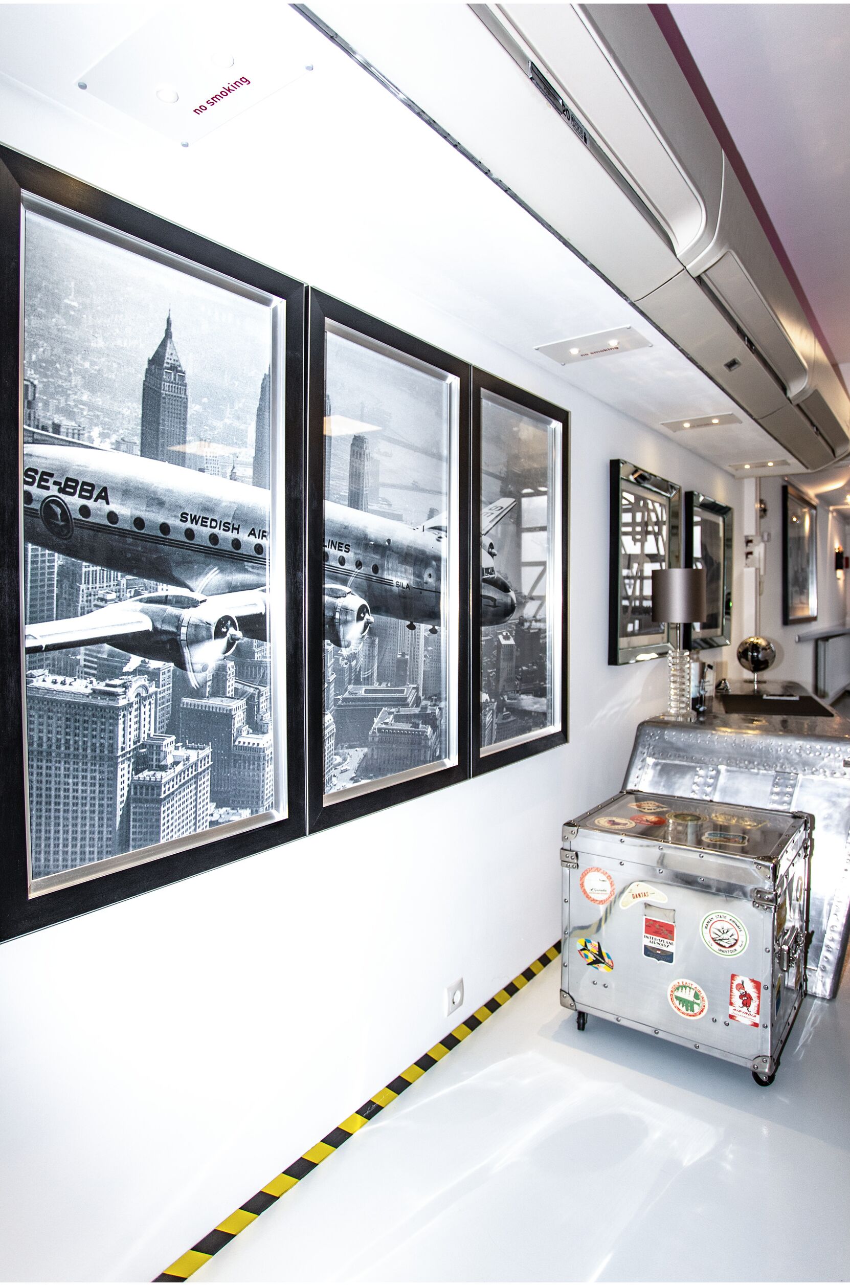 Ein modernes Interieur mit gerahmten Schwarz-Weiß-Fotos von Flugzeugen, einem metallenen Koffer mit Aufklebern und einem Rauchverbot-Schild.