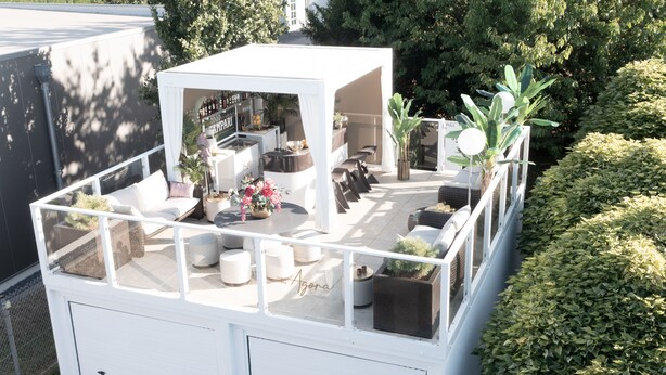 Een terras op het dak met buitenmeubels, een bar en plantenpotten.