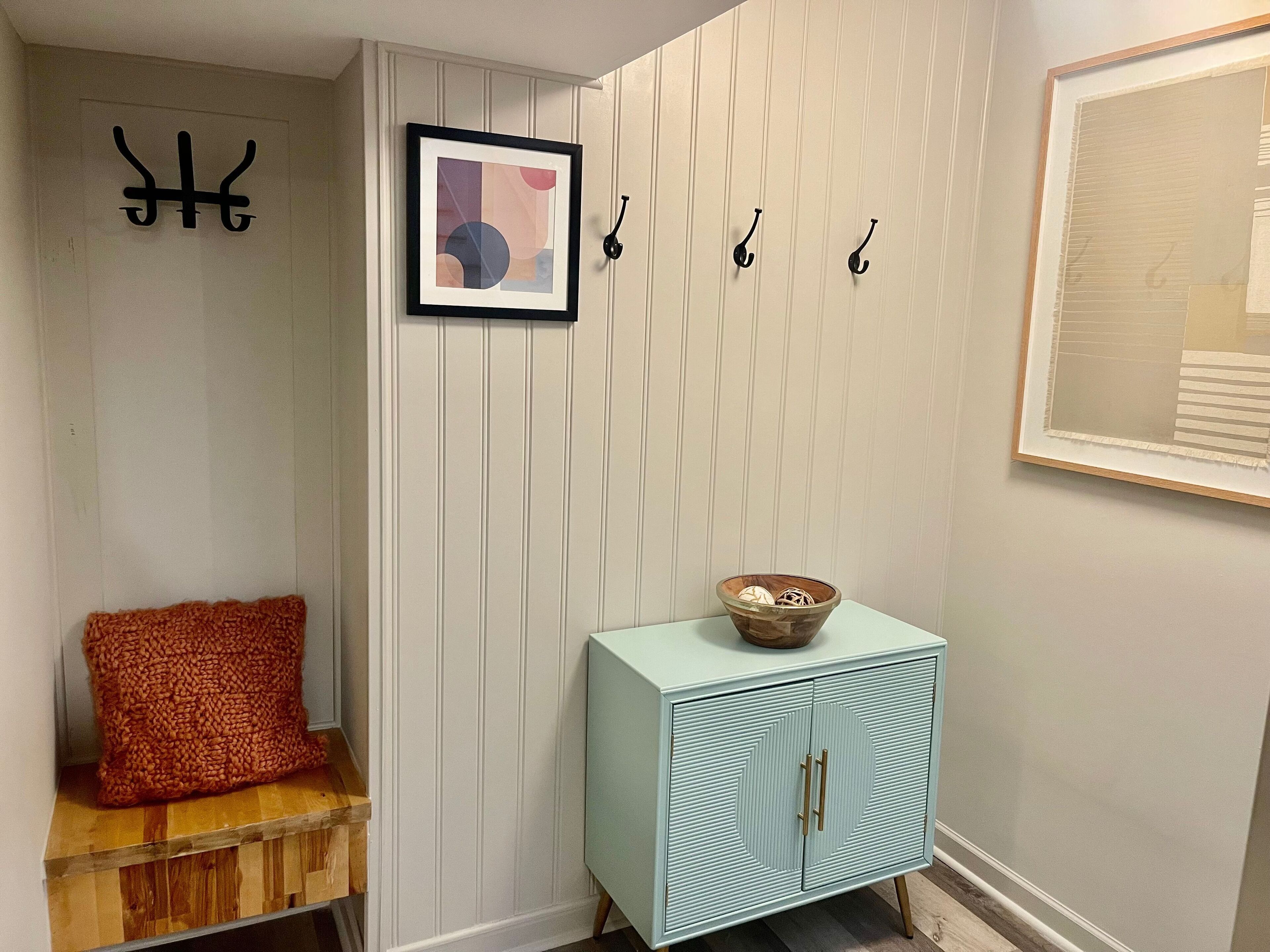 A hallway with a light blue cabinet, a framed abstract painting, and a wooden bench with a red cushion.