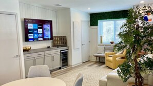 A modern kitchen with a flat-screen TV displaying streaming services, a dining area with a round table and grey chairs, and a living room with a sofa and a potted plant. - Modern Fully Renovated Loft in Downtown Trenton (Trenton)