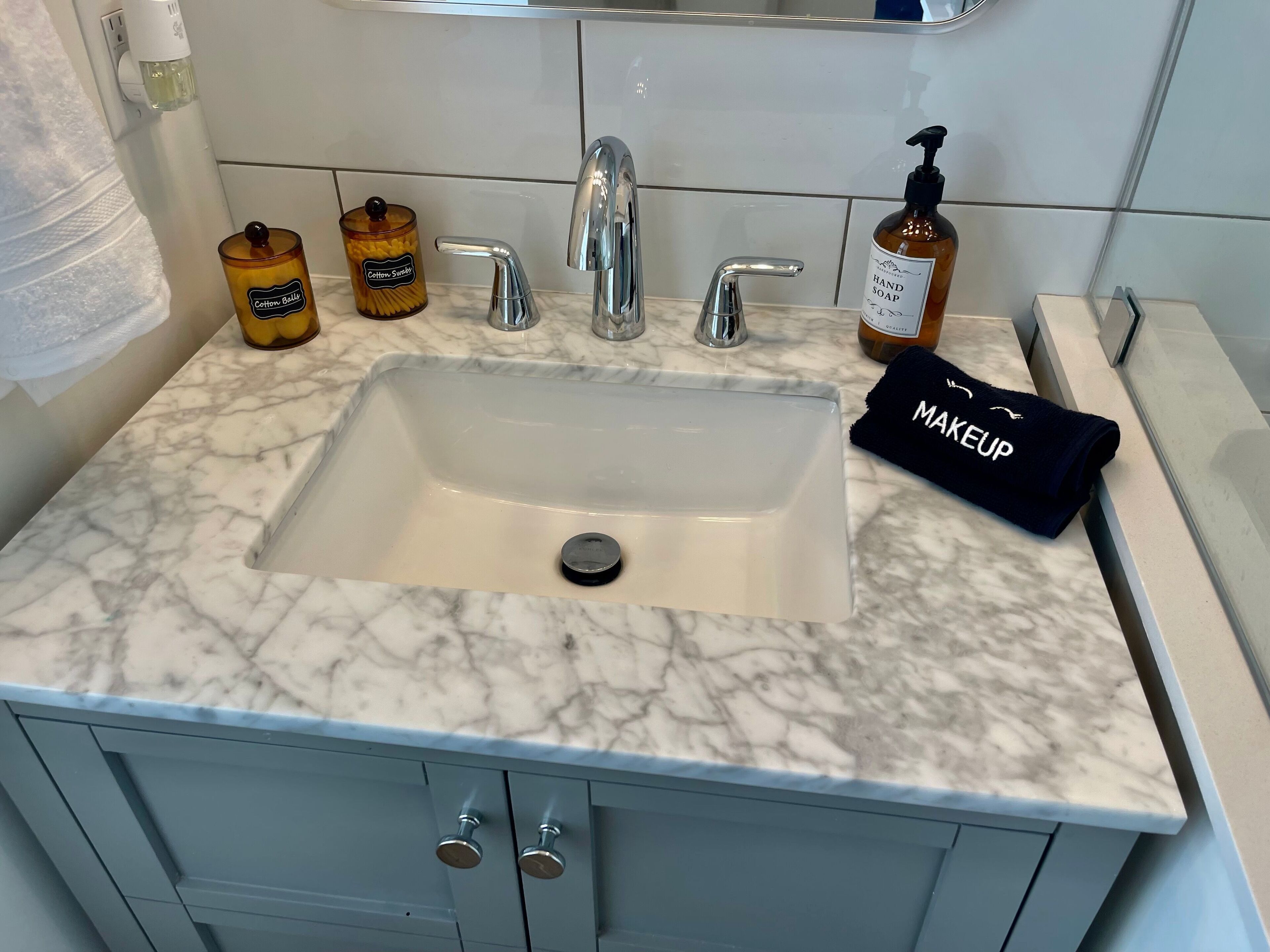 Une salle de bain avec un lavabo en marbre, deux robinets, un distributeur de savon et un pot à bonbons en forme de barbe à papa.
