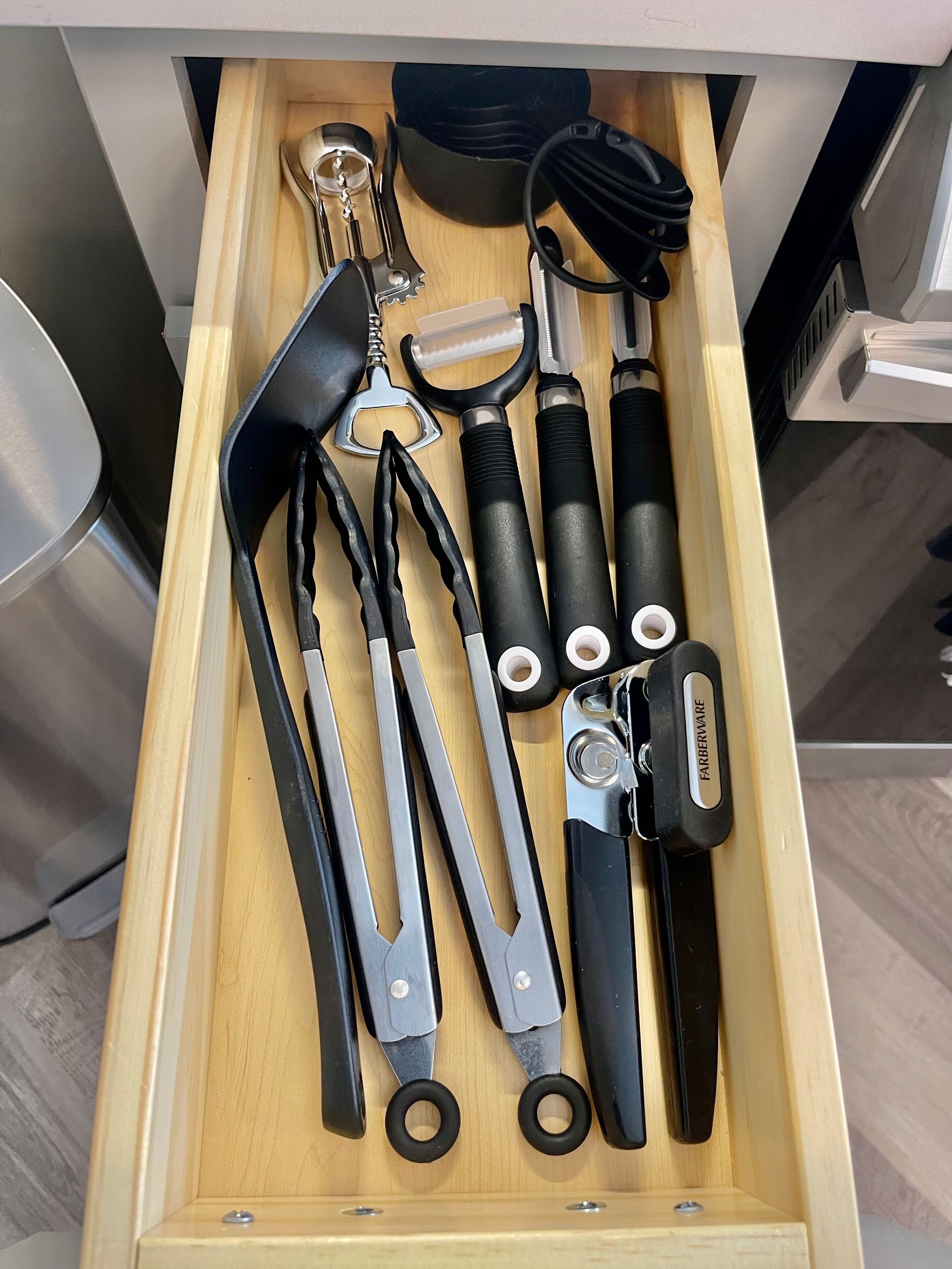 A drawer containing various kitchen utensils including a pair of scissors, a bottle opener, and a corkscrew.