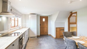 A modern kitchen with a built-in oven, a large window, and a dining area with a wooden table and chairs. - 3 bedroom accommodation in Church Stretton (Church Stretton)