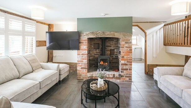 A living room with a brick fireplace, two sofas, a coffee table, and a flat-screen TV mounted on the wall. - 3 bedroom accommodation in Church Stretton (Church Stretton)